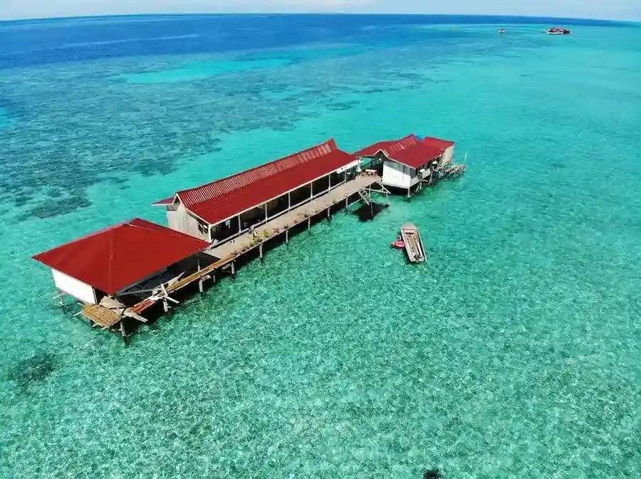 Stunning aerial drone view of the traditional wooden structure of Grand Dive Resort built over a vibrant turquoise coral reef in Semporna.