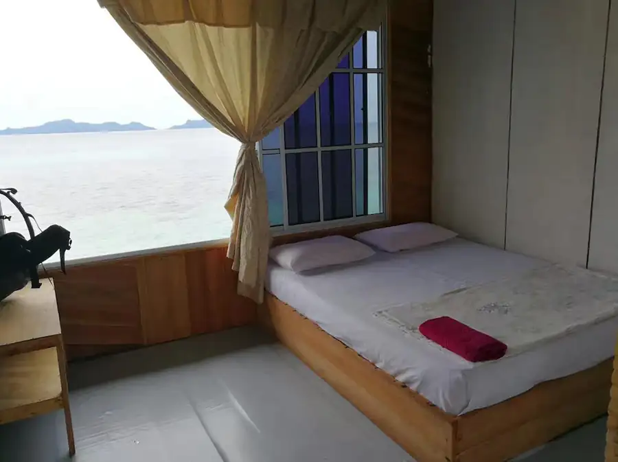 Cozy bedroom at Grand Dive Resort with a comfortable wooden bed and a large window offering beautiful ocean views.