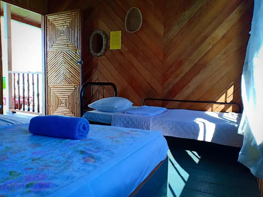 Interior of a traditional rustic room at Grand Dive Resort featuring diagonal wooden walls, a woven bamboo door, and comfortable beds.