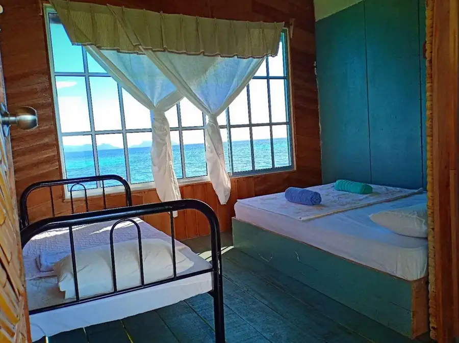 Spacious triple room at Grand Dive Resort featuring one single and one double bed, with large windows overlooking the bright blue ocean.
