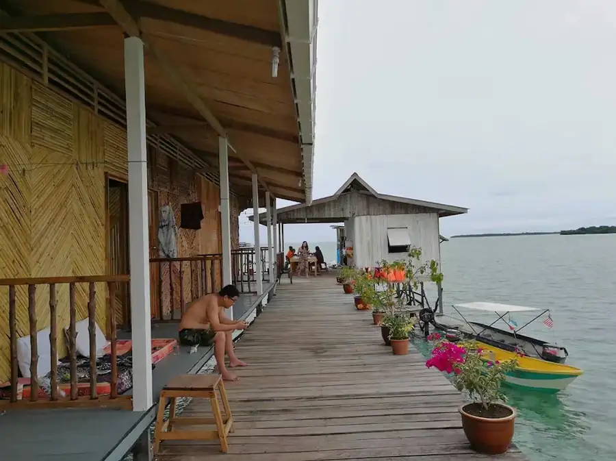 Guests relaxing on the long outdoor wooden walkway connecting the traditional bamboo water chalets at Grand Dive Resort.